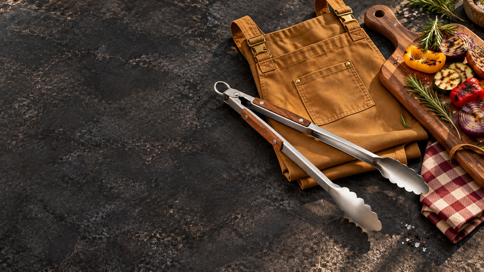 Caramel apron, wood-handled barbecue tools and serving board on a dark table